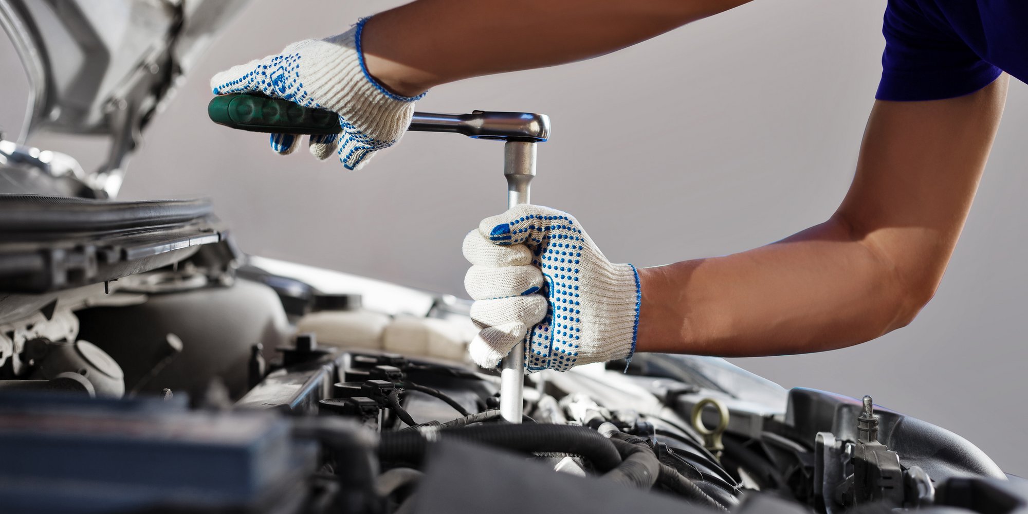 Mechaniker mit Arbeitshandschuhen repariert Motor mit Ratsche unter geöffneter Haube.